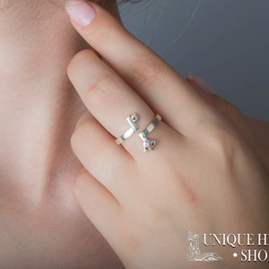 May include: A silver ring with a key design and a small purple gemstone. The ring is worn on the middle finger of a person's hand.