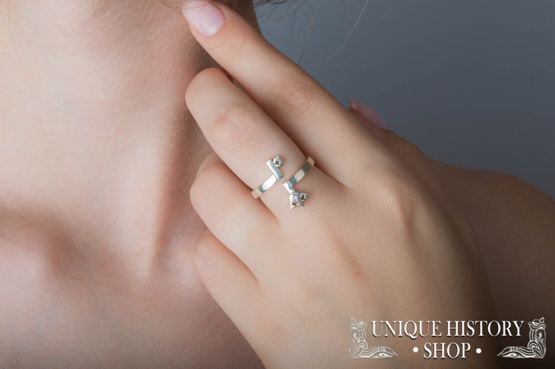 May include: A silver ring with a key design and a small purple gemstone. The ring is worn on the middle finger of a person's hand.