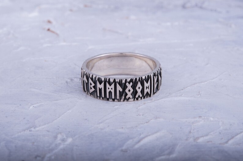 Op de afbeelding: Een zilveren ring met een zwarte inscriptie van runen rond de band.