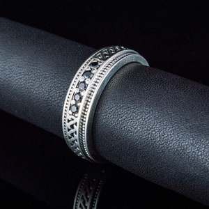 May include: A silver band ring with a row of black gemstones set in a decorative pattern.