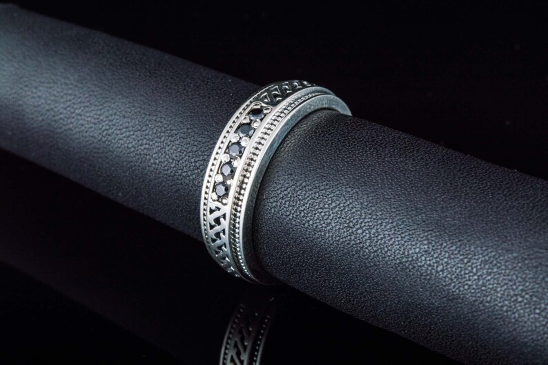 May include: A silver band ring with a row of black gemstones set in a decorative pattern.