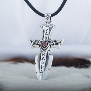 May include: Silver pendant necklace with a sword design and a red gemstone. The sword has the word "Valhalla" inscribed on it.