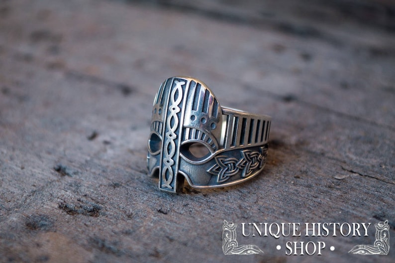 Pode incluir: Um anel de prata com um design detalhado de um capacete viking. O anel est&aacute; sobre uma superf&iacute;cie de madeira.