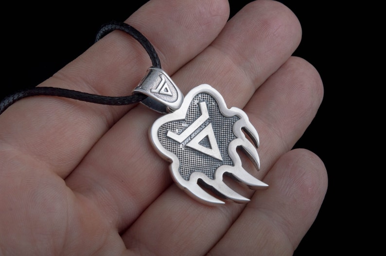 May include: Silver pendant necklace with a bear claw design and a triangle symbol inside. The pendant is on a black cord.