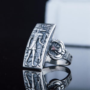 May include: Silver ring with an Egyptian god design on one side and a scarab beetle with a red stone on the other side.