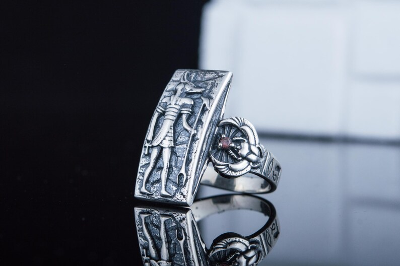 May include: Silver ring with an Egyptian god design on one side and a scarab beetle with a red stone on the other side.