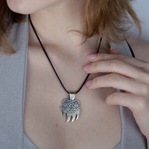 May include: A silver bear paw pendant necklace with a Celtic knot design. The necklace is on a black cord.