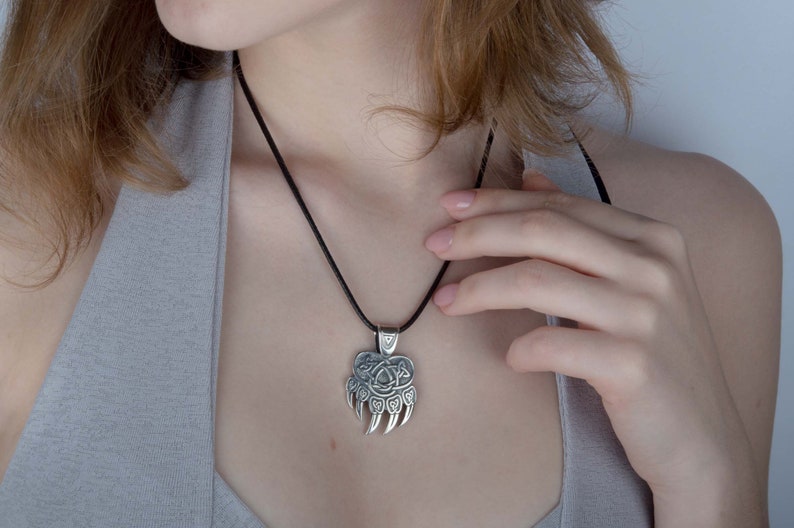 May include: A silver bear paw pendant necklace with a Celtic knot design. The necklace is on a black cord.
