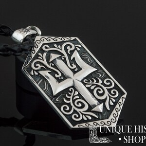 May include: Silver pendant necklace with a detailed trident design surrounded by ornate scrollwork. The pendant is attached to a black leather cord.