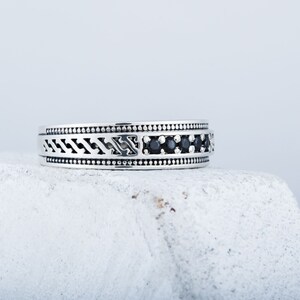 May include: A silver ring featuring a black stone inlay and intricate patterned detailing.