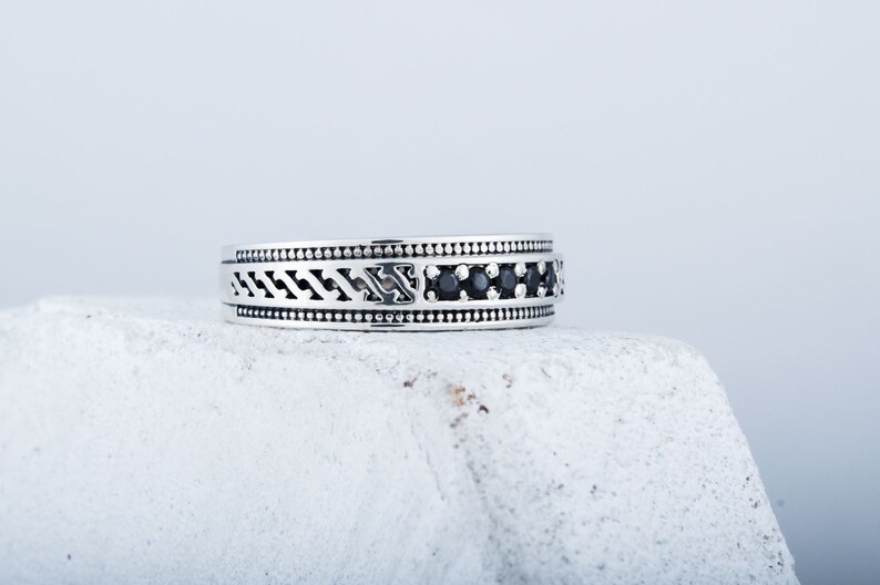 May include: A silver ring featuring a black stone inlay and intricate patterned detailing.