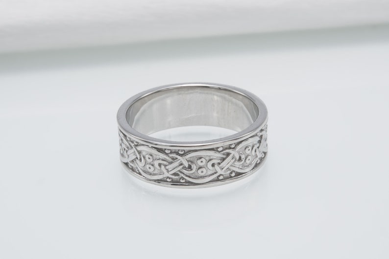 May include: A silver ring with a Celtic knot design. The knot is intricate and detailed, with small dots throughout the design.
