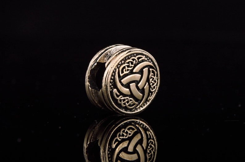 May include: A gold-colored metal bead with a Celtic knot design. The bead is round and has a hole in the center.