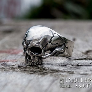 Pu&ograve; includere: Un anello d'argento a forma di teschio con dettagli elaborati. Il teschio &egrave; raffigurato con una superficie screpolata e una mascella prominente.