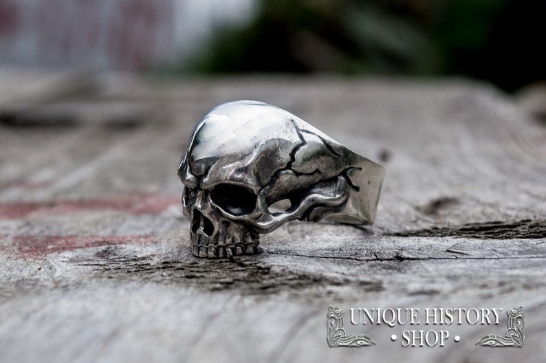 Pu&ograve; includere: Un anello d'argento a forma di teschio con dettagli elaborati. Il teschio &egrave; raffigurato con una superficie screpolata e una mascella prominente.