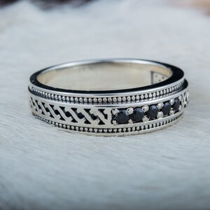 May include: A silver band ring with a black geometric design and black gemstones.