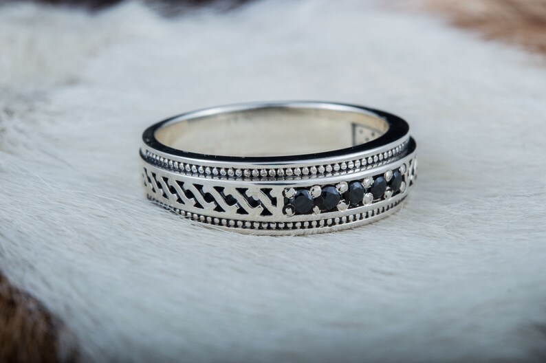 May include: A silver band ring with a black geometric design and black gemstones.