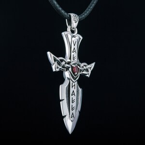 May include: Silver pendant in the shape of a sword with a red gemstone. The sword has the words "Valhalla" inscribed on it.