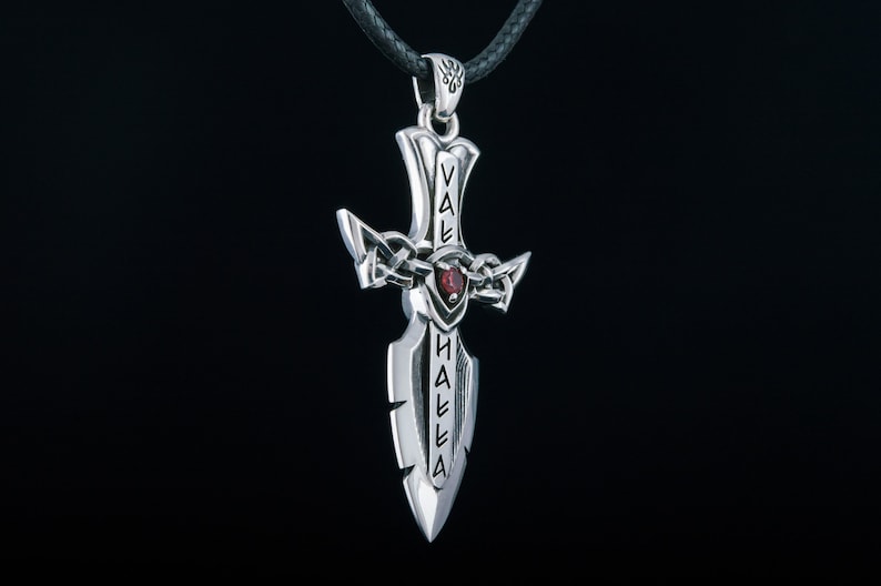 May include: Silver pendant in the shape of a sword with a red gemstone. The sword has the words "Valhalla" inscribed on it.