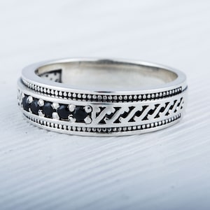 May include: A silver band ring with a black stone inlay and a decorative pattern.