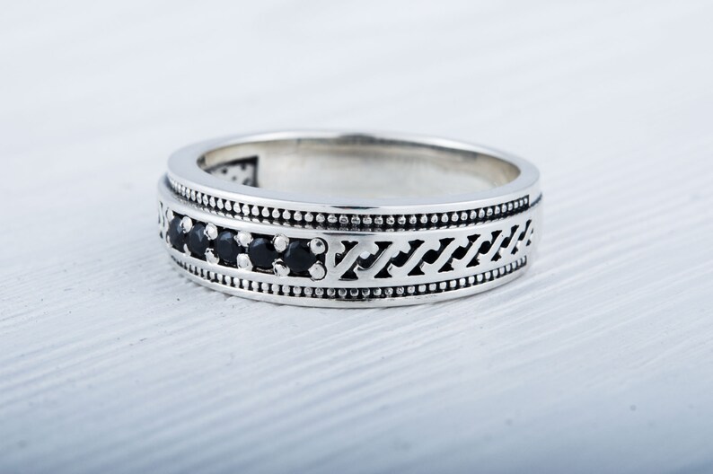 May include: A silver band ring with a black stone inlay and a decorative pattern.