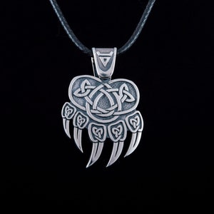 May include: Silver bear paw pendant necklace with a Celtic knot design. The pendant is on a black leather cord.