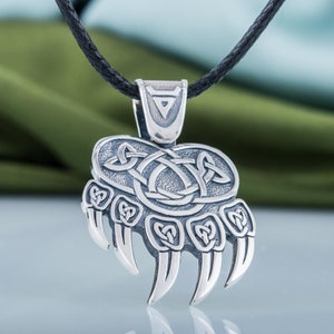 May include: Silver bear paw pendant necklace with a Celtic knot design. The pendant is on a black cord.