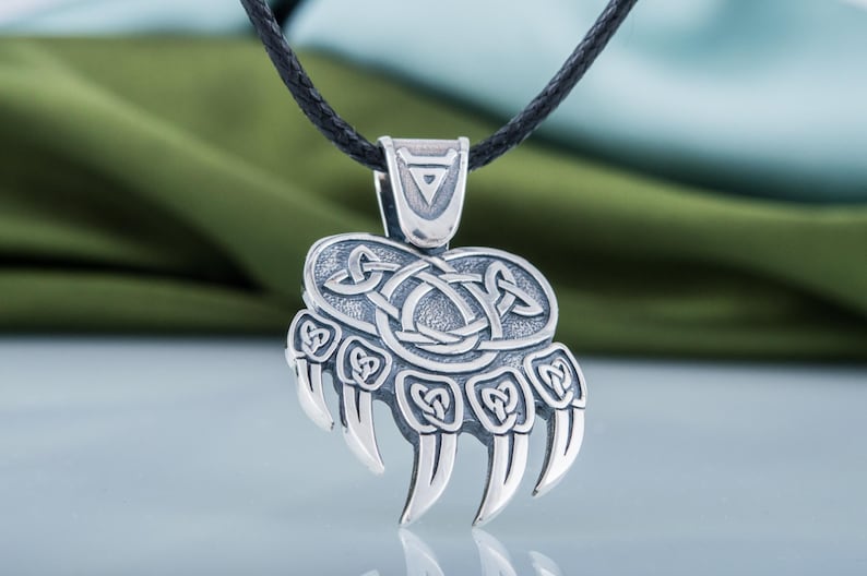 May include: Silver bear paw pendant necklace with a Celtic knot design. The pendant is on a black cord.