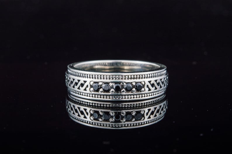 May include: A silver band ring with a decorative pattern and black gemstones.