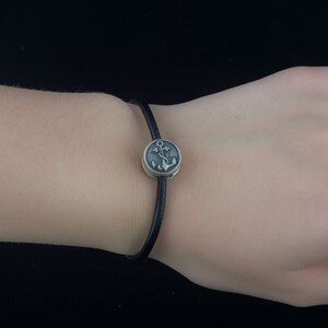 Puede incluir: Un brazalete de cuero negro con un dije de plata con dise&ntilde;o de ancla.