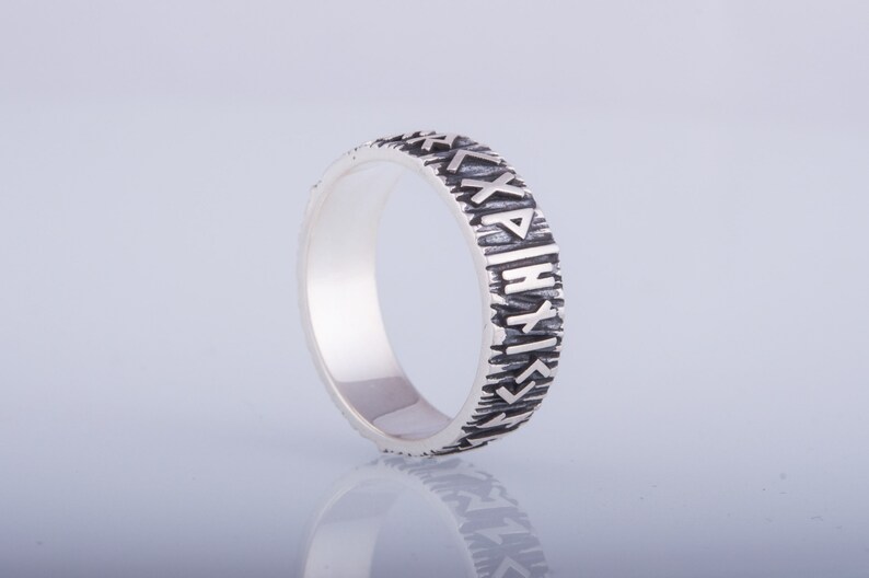 Op de afbeelding: Een zilveren ring met een getextureerde band en runen gegraveerd rond de band.