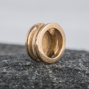 May include: A gold-colored metal bead with a circular design and a smooth, polished finish.