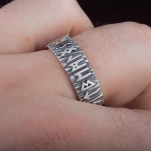 Op de afbeelding: Een zilveren ring met een getextureerde band en runen gegraveerd rond de band.
