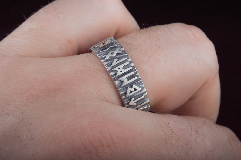 Op de afbeelding: Een zilveren ring met een getextureerde band en runen gegraveerd rond de band.