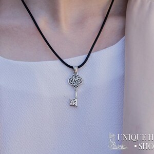 K&ouml;nnte beinhalten: Eine silberne Schl&uuml;ssel-Anh&auml;nger-Kette mit einem schwarzen Band. Der Schl&uuml;ssel hat ein filigranes Design und ist ein beliebtes Symbol f&uuml;r Hoffnung und Neuanf&auml;nge.