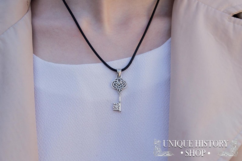 K&ouml;nnte beinhalten: Eine silberne Schl&uuml;ssel-Anh&auml;nger-Kette mit einem schwarzen Band. Der Schl&uuml;ssel hat ein filigranes Design und ist ein beliebtes Symbol f&uuml;r Hoffnung und Neuanf&auml;nge.