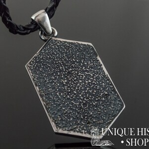 May include: Silver pendant with a textured, octagonal shape. The pendant is attached to a black leather cord.