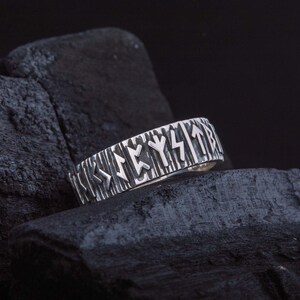 Op de afbeelding: Een zilveren ring met een getextureerd hout-achtig ontwerp en gegraveerde Noorse runen op de band.