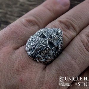 Peut inclure: Une bague en argent d&eacute;taill&eacute;e avec un motif de cr&acirc;ne et des gravures complexes. La bague est port&eacute;e au doigt, mettant en valeur le savoir-faire. Le design comprend des motifs floraux et g&eacute;om&eacute;triques. L'image comprend &eacute;galement le texte "UNIQUE HISTORY SHOP".