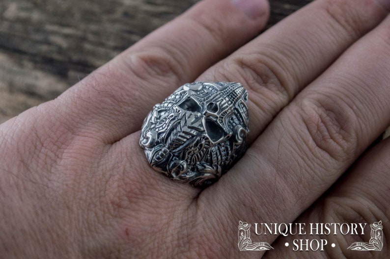 Peut inclure: Une bague en argent d&eacute;taill&eacute;e avec un motif de cr&acirc;ne et des gravures complexes. La bague est port&eacute;e au doigt, mettant en valeur le savoir-faire. Le design comprend des motifs floraux et g&eacute;om&eacute;triques. L'image comprend &eacute;galement le texte "UNIQUE HISTORY SHOP".