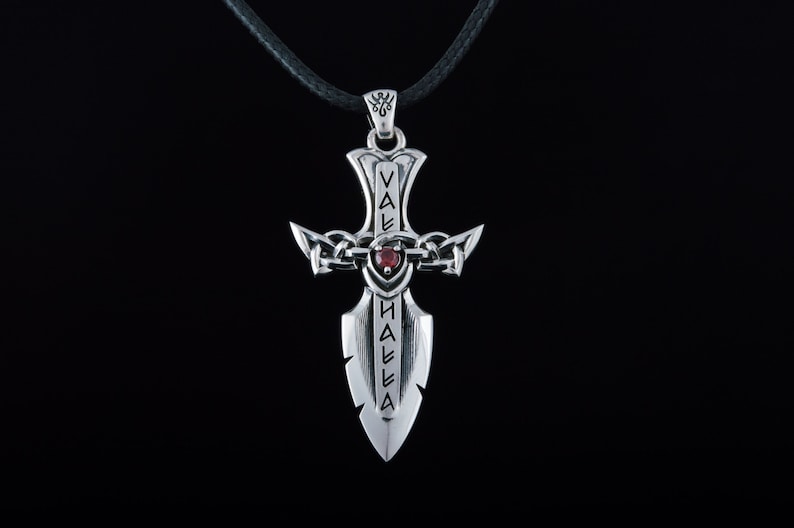 May include: Silver pendant necklace with a sword design featuring a red gemstone and the inscription "Valhalla".