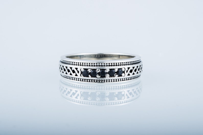 May include: A silver band ring with a black stone inlay and a decorative pattern. The ring is on a white background.