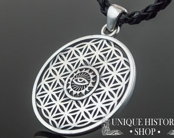 Puede incluir: Collar con colgante de plata, de diseño circular, adornado con un patrón de flor de la vida y un ojo que todo lo ve en el centro. El colgante está unido a un cordón de cuero negro.