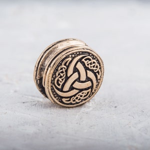 May include: A gold-colored metal bead with a Celtic knot design featuring a triskelion symbol.