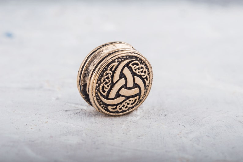 May include: A gold-colored metal bead with a Celtic knot design featuring a triskelion symbol.