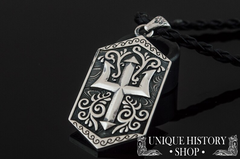 May include: Silver pendant necklace with a trident design. The pendant is detailed with intricate floral patterns and a black leather cord.