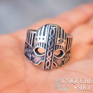 Pode incluir: Um anel de prata com um design detalhado de um capacete viking. O anel est&aacute; na m&atilde;o de uma pessoa.