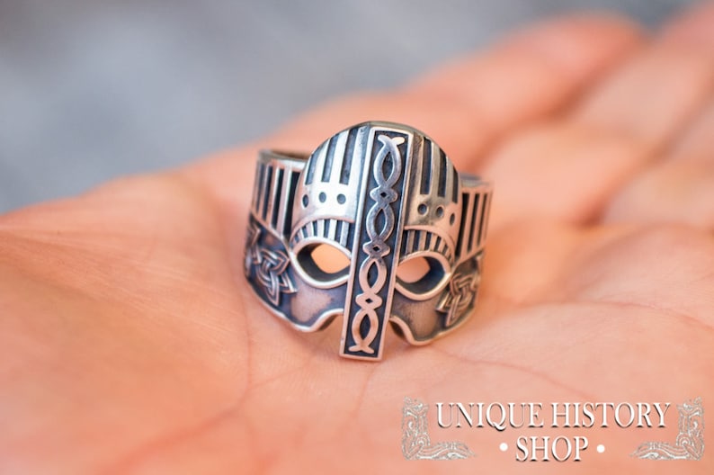 Pode incluir: Um anel de prata com um design detalhado de um capacete viking. O anel est&aacute; na m&atilde;o de uma pessoa.