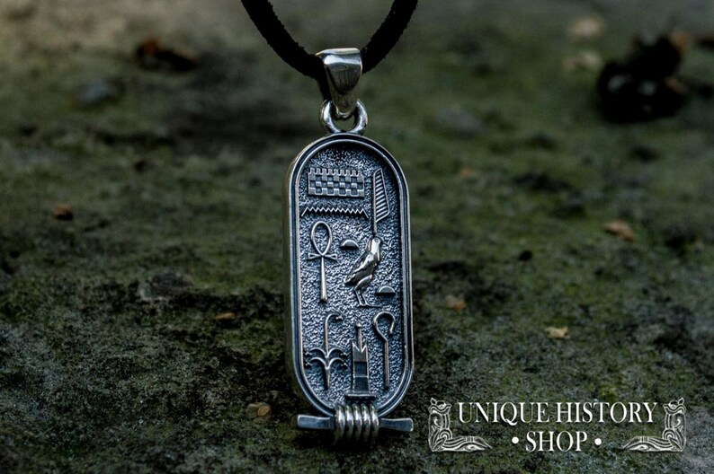 May include: Silver pendant necklace with an Egyptian scarab design. The pendant features a winged scarab beetle, an ankh symbol, and other hieroglyphs. The pendant is on a black cord.