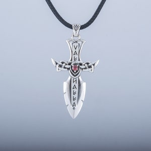 May include: Silver pendant necklace featuring a sword design with a red gemstone. The sword has the word "VALHALLA" inscribed on it.
